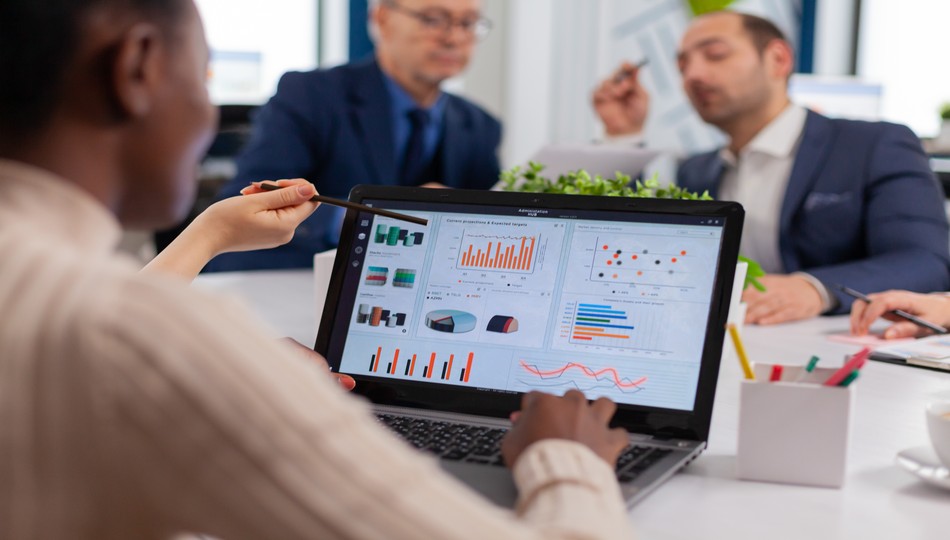 Team member pointing a pencil at a laptop showing business intelligence dashboards with charts and graphs during a meeting, representing business intelligence consulting