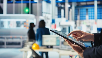 Factory worker using a tablet to monitor production systems on a manufacturing floor, representing IT/OT convergence in manufacturing modernization