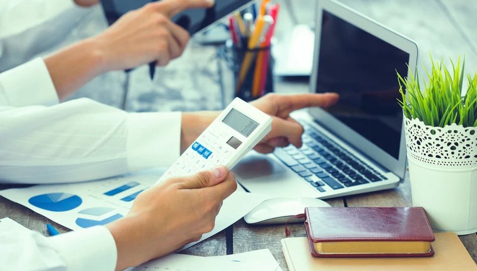 Outsourcing cost savings illustrated through hands using a calculator, laptop, and financial charts.