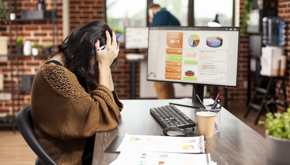 Outsourcing product development fails shown through a stressed woman at her desk with data dashboards.