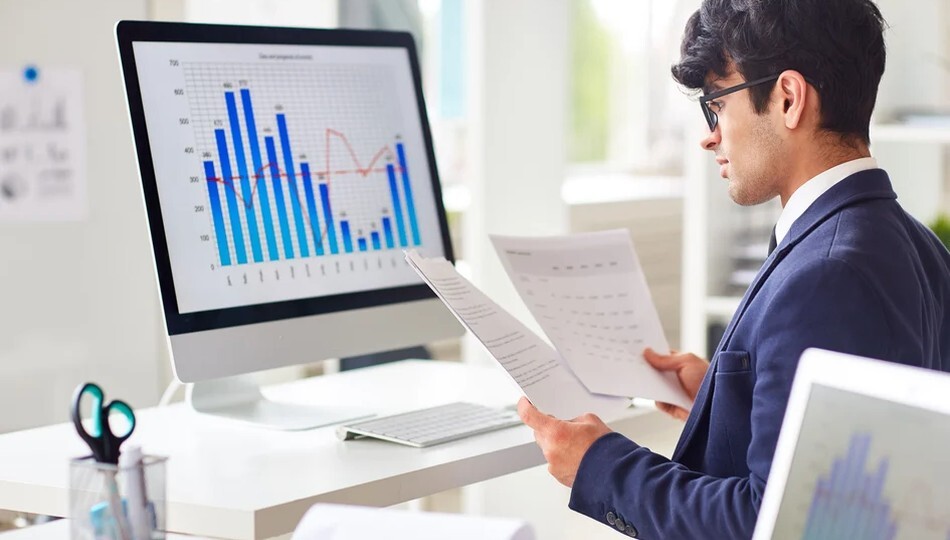 Software development cost estimation shown through a businessman reviewing charts on a computer screen.