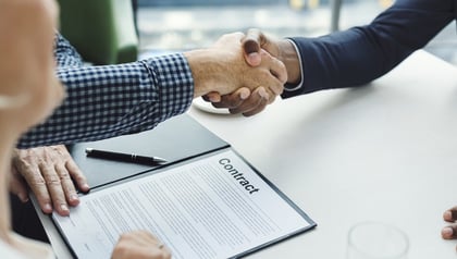 Software outsourcing contract signing shown through a handshake over a signed agreement document.