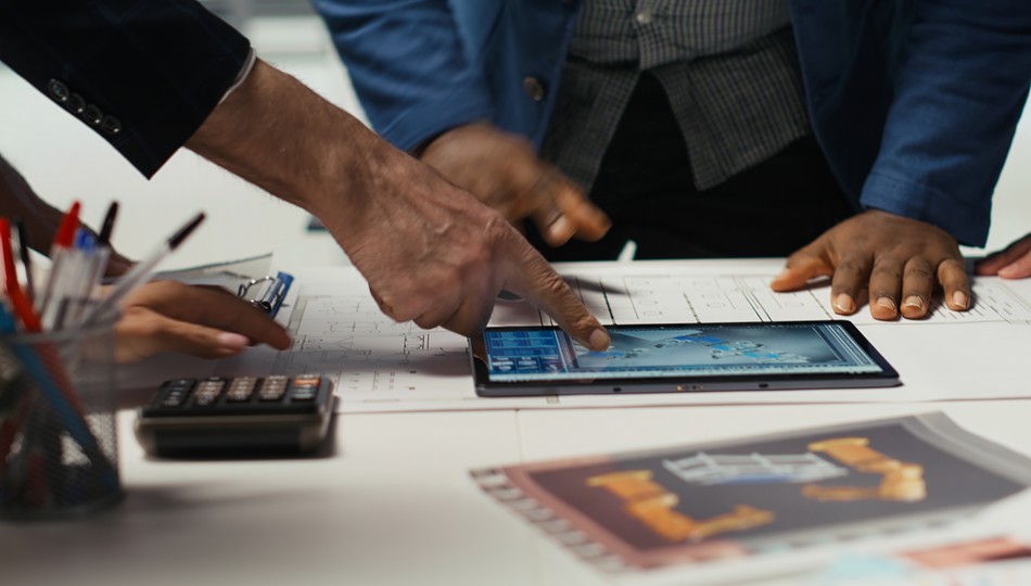 Team reviewing CAD blueprints and a tablet with technical drawings, discussing application modernization strategy