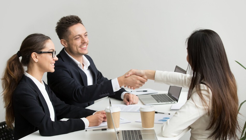 SaaS customer retention shown by business partners shaking hands across a meeting table.