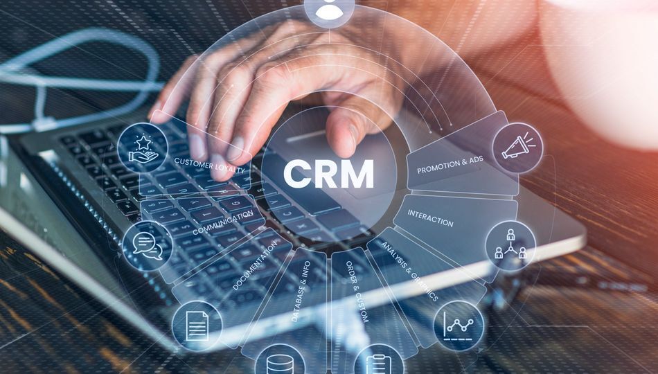 Custom CRM development shown by a hand typing on a laptop with a CRM diagram of customer icons.